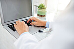 Unknown mixed race woman using a laptop and typing a email while sitting at her desk in a hospital. Female doctor using a wireless device while working