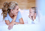 Happy caucasian mother and daughter lying on a bed at home. Cheerful woman with cute little girl enjoying a cosy and lazy relaxing day together. Loving parent bonding and sharing quality time with kid