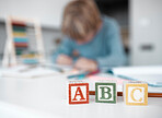 Closeup of wooden toy blocks on a table at home. A little boy blurred in the background, playing, doing his homework and getting an education through distance learning