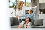 Happy caucasian family bonding at home. Excited little boy sitting on his father's shoulders and holding his mother's hands while pretending to fly for play and fun. Loving parents relaxing with son 