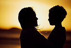 Silhouette shot of a mother holding her son on the beach at sunset. Woman and kid spending time together at the beach against golden sky. Mom and son sharing a beautiful bond