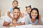 Portrait of a cheerful family lying together on bed. Little boy and girl lying on their parents laughing and having fun. Mixed race couple bonding with their son and daughter. Hispanic siblings enjoying free time with their mother and father