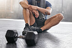 Closeup of one active caucasian man taking a break from exercise in a gym. Masculine guy with tattoos sitting on the floor after training with dumbbell weights in a fitness centre