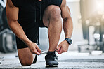 Unknown trainer tying shoelaces alone in gym. One mixed race coach kneeling and getting ready to workout health club. Hispanic man crouching down in fitness centre before routine exercise and training