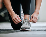 Closeup of unknown trainer tying shoelaces alone in gym. One caucasian coach kneeling, getting ready to workout health club. Woman crouching down in fitness centre before routine exercise and training