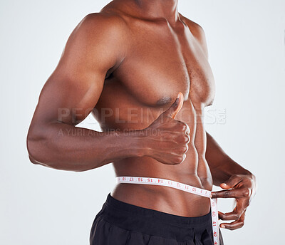 Buy stock photo Black man, waist and thumbs up with measuring tape for weightloss or diet on a gray studio background. Muscular African, male person or model with like emoji, yes sign or OK for size or fitness goals