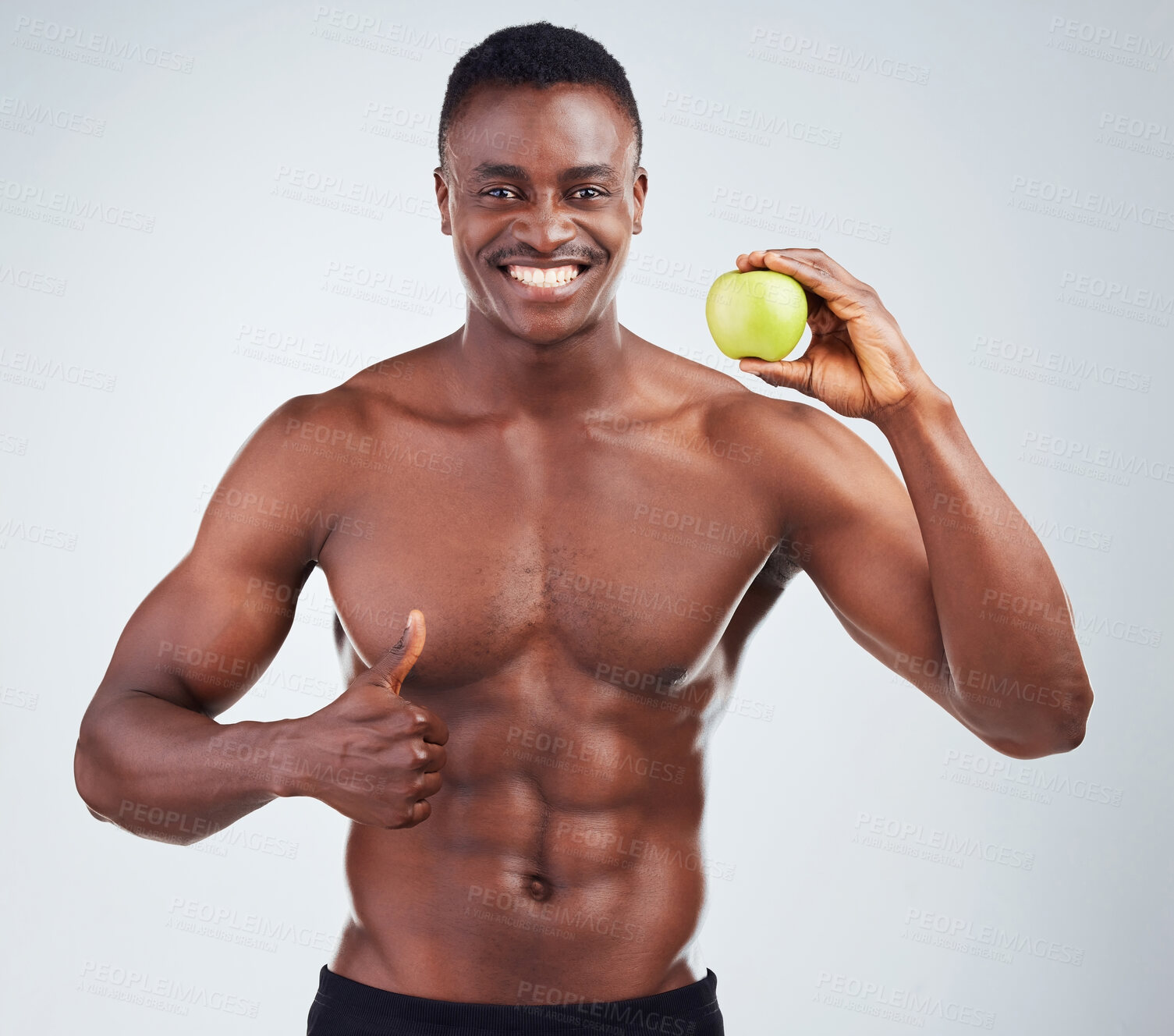 Portrait of a smiling African American fitness model posing topless with an  apple and looking muscular. Happy black male athlete isolated on grey  copyspace showing the thumbs up to a healthy diet |