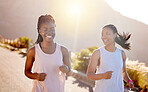 Two happy young female athletes out for a run on a mountain road on a sunny day. Energetic young women running outdoors to help their bodies in shape and fit. Two diverse female friends exercising together