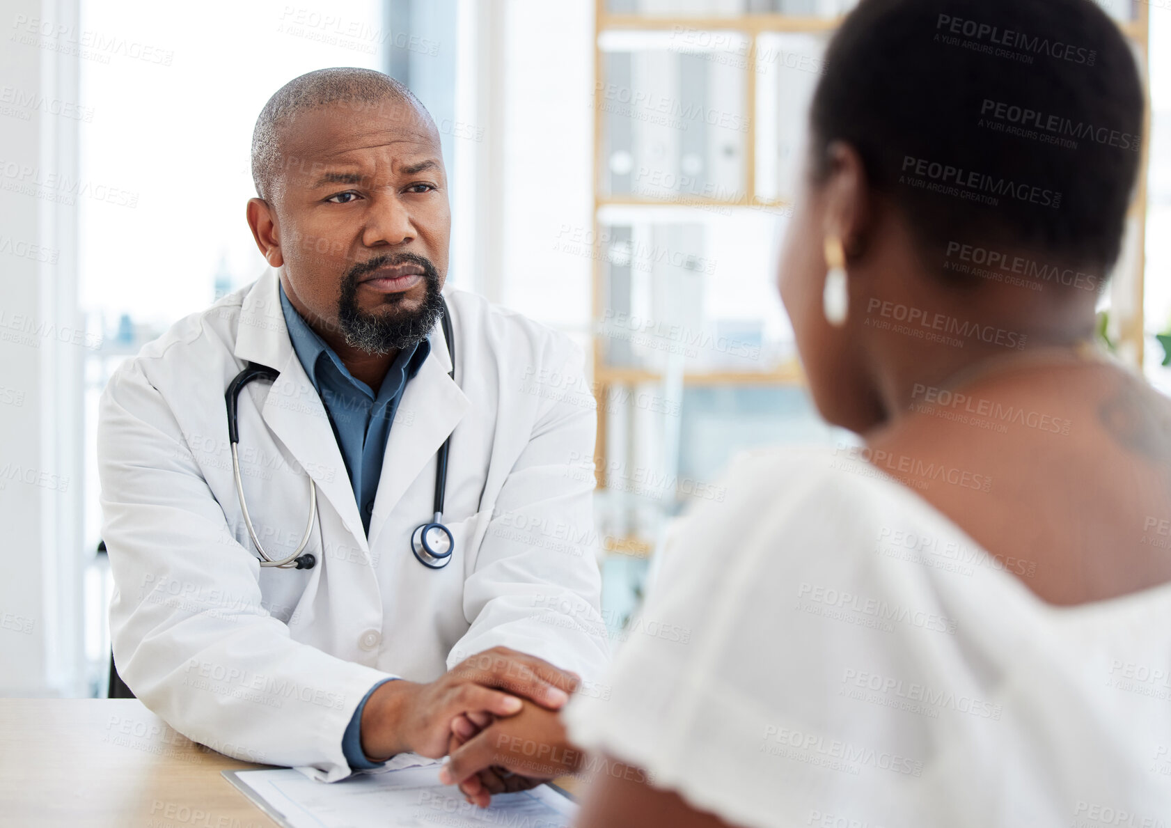 Buy stock photo Serious doctor, patient and holding hands in consultation for bad news, cancer diagnosis or comfort. Healthcare, black man and medical professional with woman for help, support and empathy in clinic.