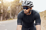 One athletic young man cycling outside. Sporty fit male wearing helmet and glasses while riding a bike on a road along the mountain for exercise. Endurance and cardio during a workout and training