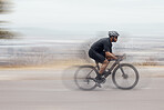 One athletic young man cycling fast outside. Sporty fit male wearing helmet and glasses while riding a bike long distance with speed during a race. Endurance and cardio during a workout and training