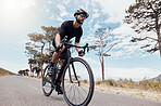 One athletic young man cycling outside. Sporty fit male wearing helmet and glasses while riding a bike on a scenic mountain road with the sky in the background for exercise