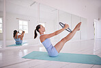 Strong woman training her core in yoga class. Young woman using equipment to train her abs. Dedicated, fit woman in pose in yoga studio. Caucasian woman sitting on the floor in yoga studio.