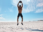 A handsome young african american male athlete working out on the beach. Dedicated black man exercising with a medicine ball outside on the sand. Committed to a healthy lifestyle and getting fit