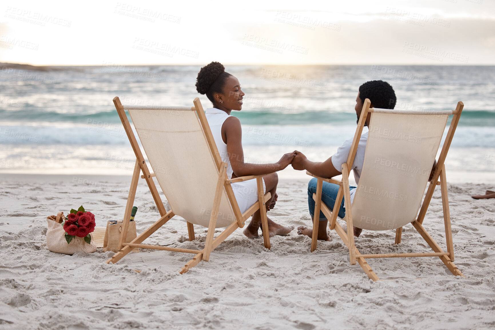 Buy stock photo Sunset, couple and holding hands with beach chair, fun or celebrating together for anniversary. Vacation, picnic and people travel for marriage on honeymoon, summer holiday and happy bonding in Miami