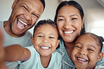 Cute little boy holding phone and taking selfie or recording funny video with his family. Happy mixed race family with two children and parents posing together for a family picture on a mobile phone