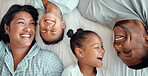 Happy laughing mixed race family with two children relaxing and lying together on a bed at home, from above. Faces of little brother and sister spending time with their loving parents