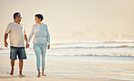 A senior mixed race couple walking together on the beach  smiling and laughing on a day out at the beach. Hispanic husband and wife looking happy and showing affection while having a romantic day on the beach