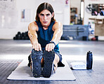 Portrait of one young caucasian man stretching for warmup to prevent injury while training in a gym. Focused guy bending to touch his feet while sitting on a mat on the floor during a workout in a fitness centre