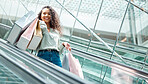 Portrait beautiful mixed race woman standing on an escalator while shopping in a mall. Young hispanic woman carrying bags, spending money, looking for sales and getting in some good retail therapy