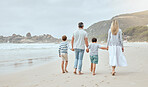 Happy caucasian parents and kids from the back holding hands while walking together along the beach shore during a relaxing fun family summer vacation. Loving mom and dad enjoying leisurely stroll while bonding with little sons