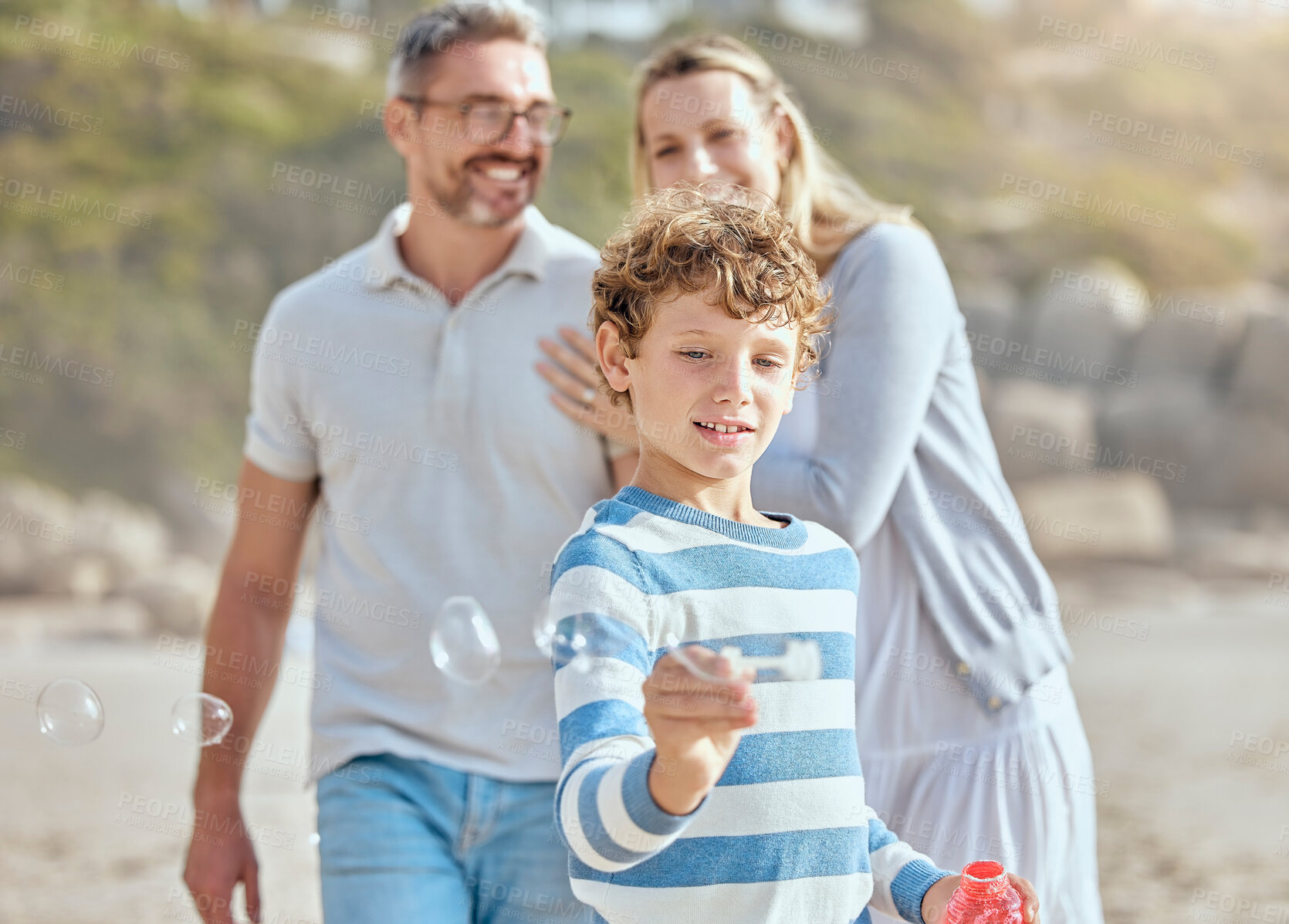 Buy stock photo Boy, bubbles and fun in vacation, parents and break in beach for family, bonding and fun for child. Outdoor, man and woman with smile for kid, proud and travel with youth in nature, mother and dad