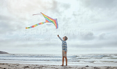 Buy stock photo Boy, child and kite by ocean for vacation, playful and outdoor in wind by waves, clouds and walk at beach. Kid, toys and rainbow fabric for flight, games and holiday by sea with adventure in Spain