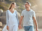 Happy and loving mature caucasian couple enjoying a romantic walk at the beach together on a sunny day. Cheerful affectionate husband and wife holding hands while bonding on vacation outdoors