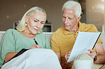 Unhappy elderly couple sitting on a sofa together and looking stressed. Senior caucasian man and woman looking worried about their future while looking at paperwork and their debt