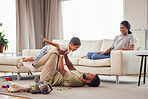 Adorable little boy being lifted in the air by his dad. Excited little male having fun and playing with his father and mother  at home. Mixed race family having fun on the couch at home