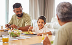 Closeup of a mixed race male and his son enjoying some food at the a table during lunch at home in the lounge. Hispanic father smiling and eating alongside his son at home