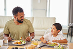 Closeup of a mixed race male and his son enjoying some food at the a table during lunch at home in the lounge. Hispanic father smiling and eating alongside his son at home