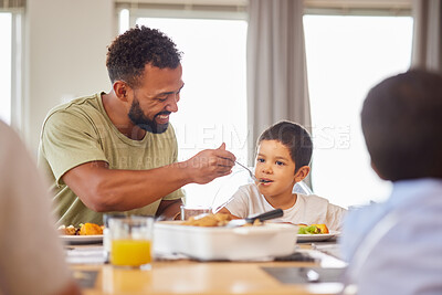 Buy stock photo Lunch, family and father feeding son at dining room table in home for meal or social gathering. Eating, food and help with smile of happy people in apartment together for bonding, diet or nutrition