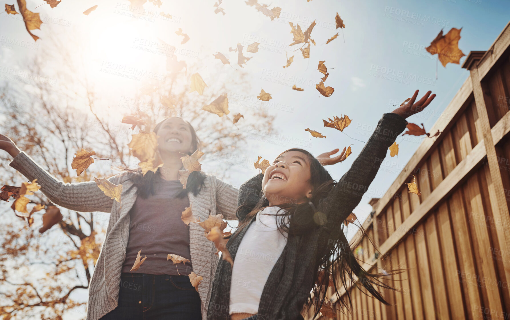 Buy stock photo Autumn, mother and daughter throwing leaves in garden of home together for bonding or love. Asian family, fall or season with single parent woman and girl child having fun in backyard for wellness