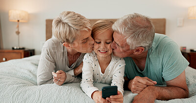 Buy stock photo Grandparents, kissing and mobile phone with grandchild in bedroom for growth, development and gaming in home. Girl, happy and tech for learning, joy and fun as youth, kid or young person with bonding