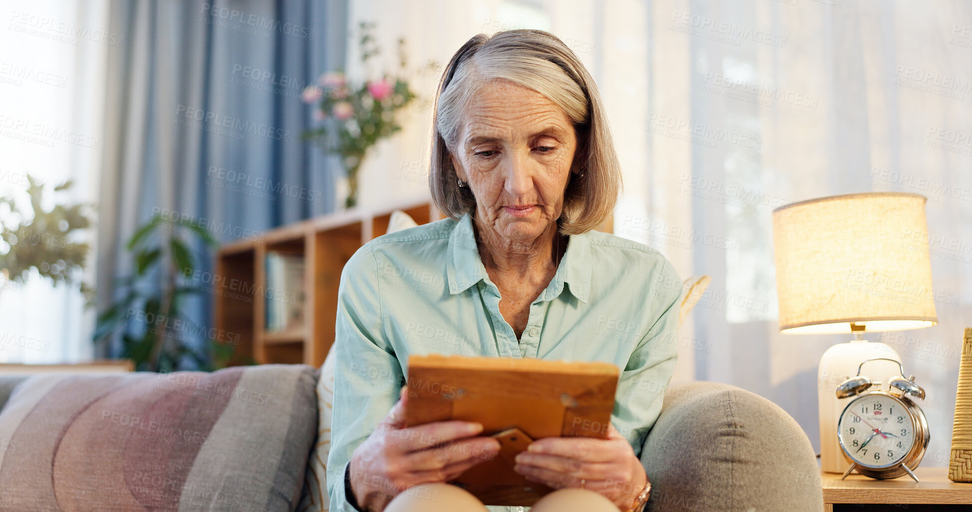 Buy stock photo Sad, senior woman and picture frame for nostalgia, memory and remember history in home living room. Retirement, photo and past of missing person with grief, lonely and mourning family member on sofa