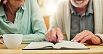 Bible, hands and study with senior couple drinking tea at table in apartment together for belief or faith. Book, Jesus or God with man and woman reading in retirement home for Christian religion