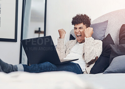 Buy stock photo Shot of a young man cheering while using a laptop on his bed at home