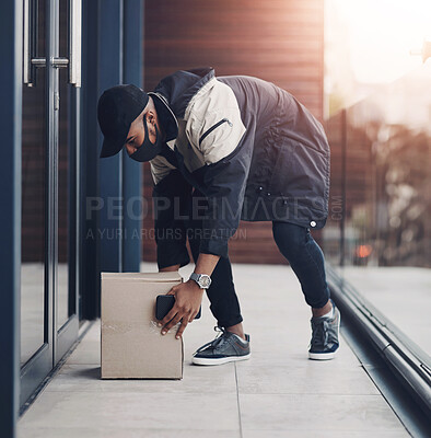 Buy stock photo Shot of a masked young man delivering a package to a place of residence