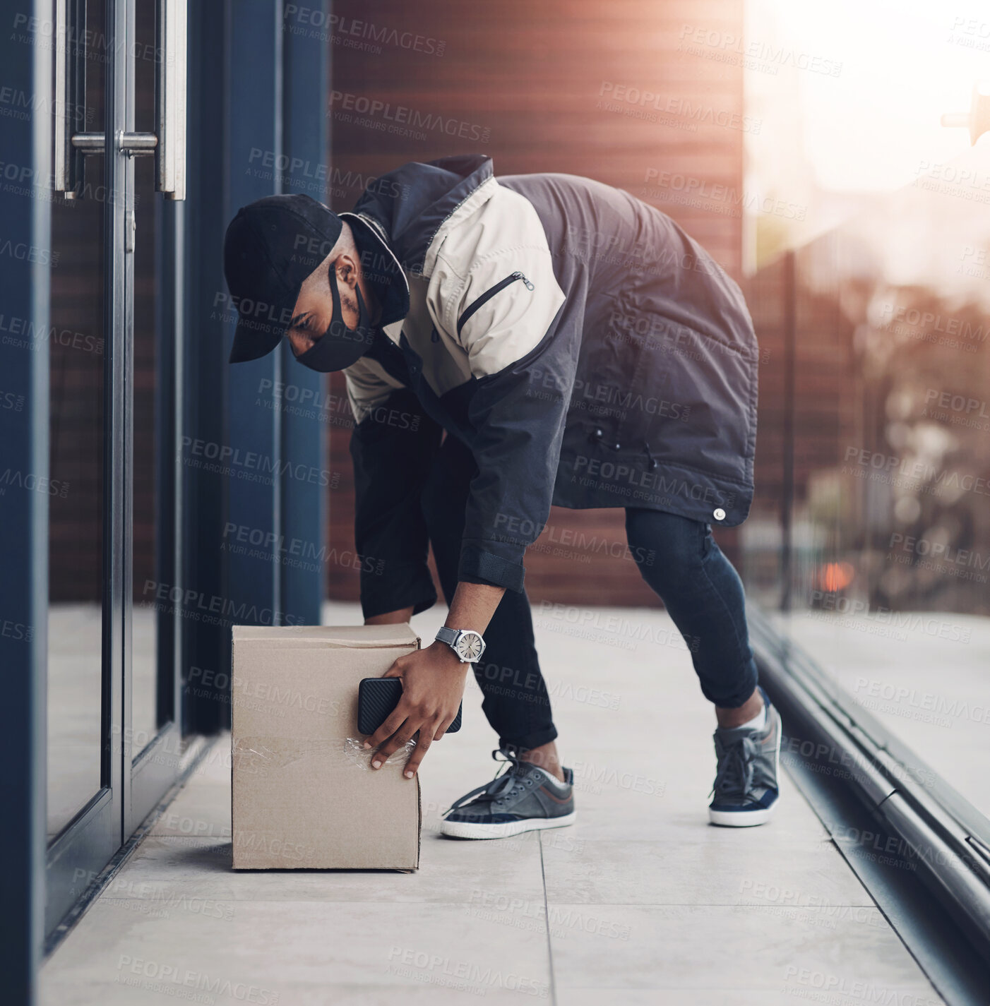 Buy stock photo Shot of a masked young man delivering a package to a place of residence