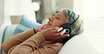 Retirement, senior woman and sofa with headphones, relax and calm in living room, streaming music and audio. Rest, happy and mature lady with headset for podcast, radio and carefree on couch