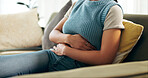 Hands, home and woman with stomach cramps, sick and pain with disease, tummy ache and virus. Closeup, person and girl on couch, illness and tired with digestion, constipation and touching abdomen