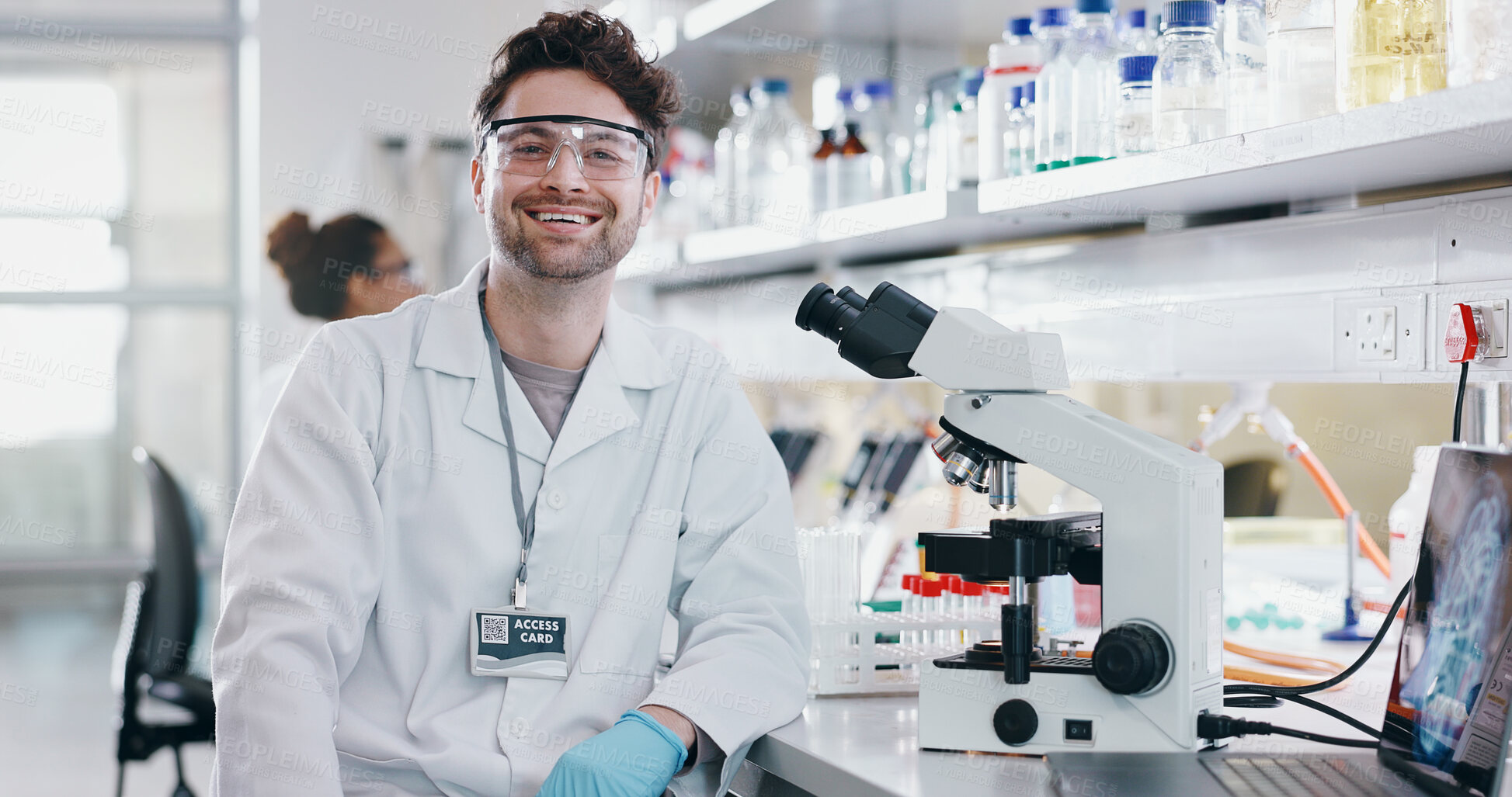 Buy stock photo Portrait, scientist and happy man on microscope in lab for chemistry research, test or innovation. Laptop, science or confident face of medical doctor in goggles for microbiology, healthcare or study