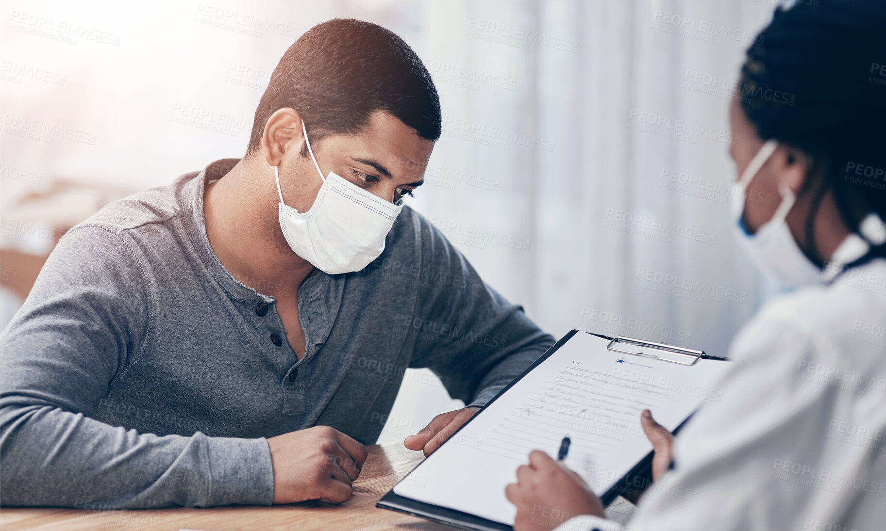 Buy stock photo Shot of a young man going through paperwork during a consultation with a doctor