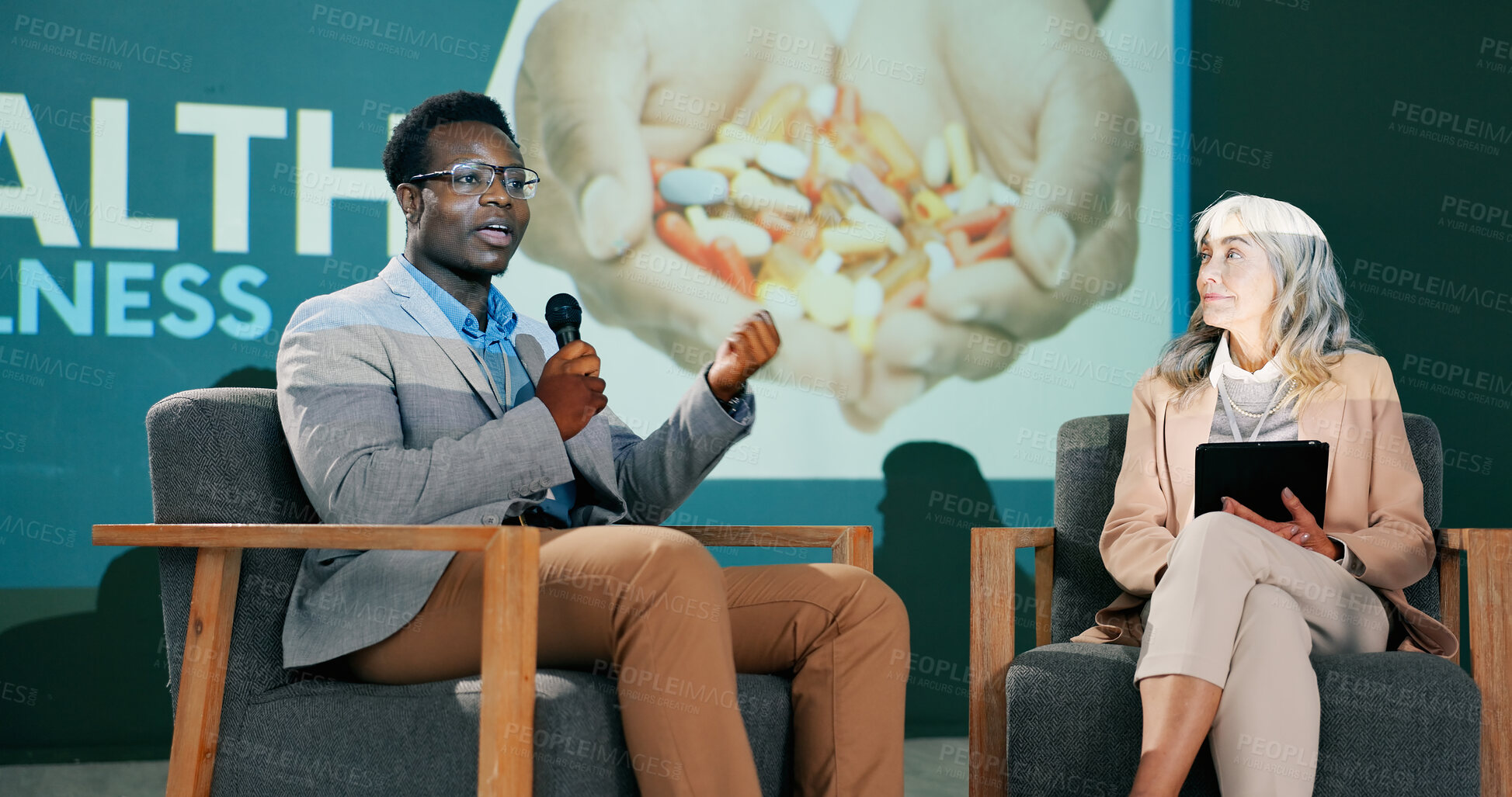 Buy stock photo Speaker, wellness conference and speech of man on stage with host on mic and tablet at event. Workshop, talking and seminar presentation on health, pharma and medical innovation of drugs with guest