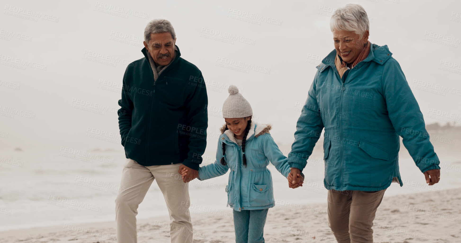 Buy stock photo Grandparents, child and beach with holding hands, happy and together on vacation by the sea. Love, smile and girl kid with senior people outdoor in winter on holiday with retirement and travel