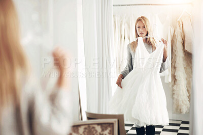 Buy stock photo A young bride looking at her reflection in a mirror while choosing a dress