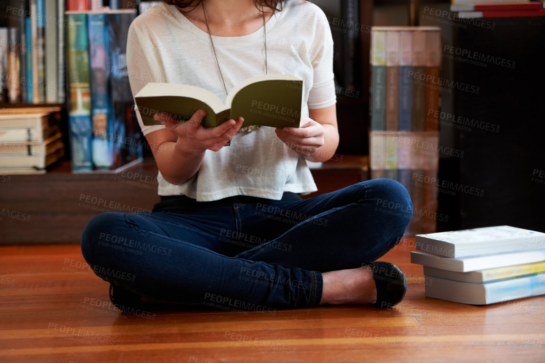 Buy stock photo A cropped shot of a young woman sitting on the floor of a bookshop and reading