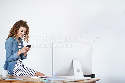 Buy stock photo Shot of a young woman using a cellphone while sitting on her desk in an office