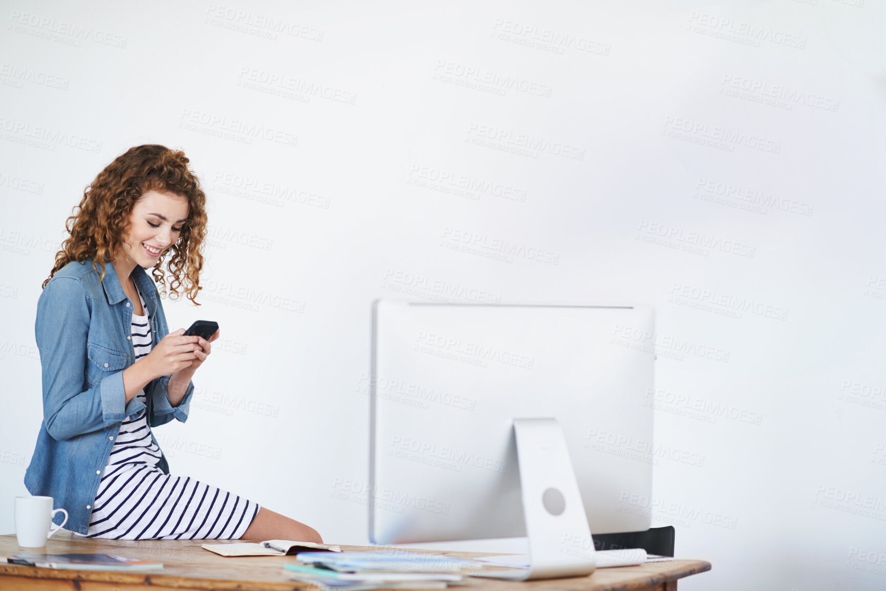 Buy stock photo Shot of a young woman using a cellphone while sitting on her desk in an office